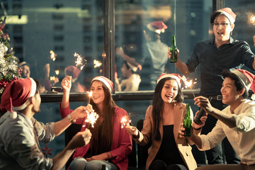 Group of diversity people having great Christmas party in working office together at night. They celebrate with beer and holding sparklers feeling happy and enjoy laughing. Xmas, new year concept