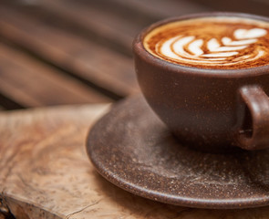 A beautiful creamy brown warm fresh cappuccino coffee cup, full of creamy coffee, served in a wooden rustic brown coffee shop with coffee art. Organic fair trade coffee photographed from above top 