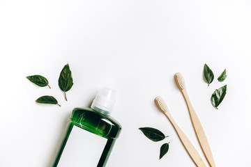 Oral care products. Mouthwash, two wooden bamboo eco friendly toothbrushes, green leaf on white background. Teeth hygiene concept. Flat lay, copy space