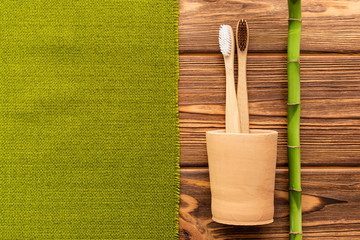 Bamboo toothbrushes in hand made clay glass bamboo plant with green towel on wooden background.Flat lay copy space. Biodegradable natural bamboo toothbrush. Eco friendly, Zero waste, Dental care