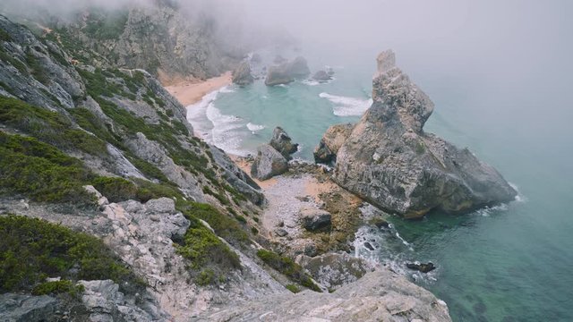 4K view from above of Rocks in morning fog at Praia da Ursa beach in Sintra, Portugal