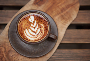 A beautiful creamy brown warm fresh cappuccino coffee cup, full of creamy coffee, served in a wooden rustic brown coffee shop with coffee art. Organic fair trade coffee photographed from above top 