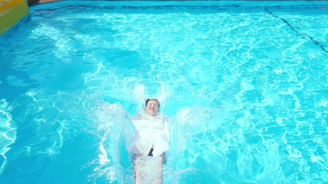 Young woman in white tunic falling on her back into the swimming pool with a clean blue water. Vacation and resort concept.