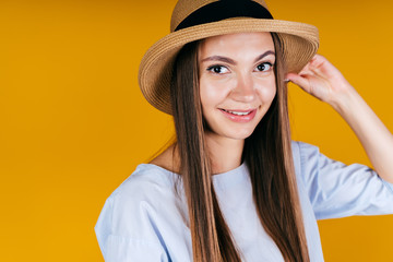 the girl with mischief in gaze and smile holds the edge of her hat with her hand. background yellow