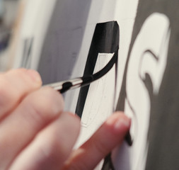 An artists hand with a paint brush painting retro letters and typography graphics. Artists hand...