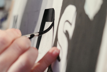 An artists hand with a paint brush painting retro letters and typography graphics. Artists hand...