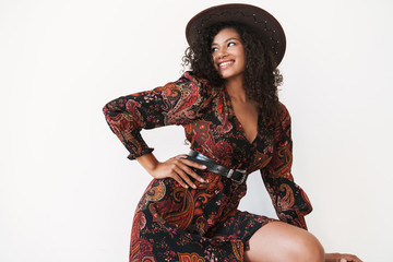 Image of young african american cowgirl in dress and hat standing by chair
