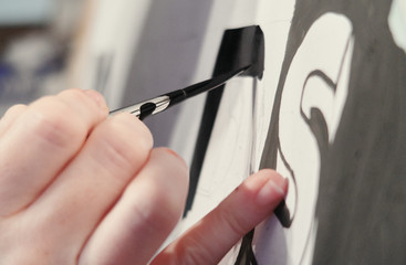 An artists hand with a paint brush painting retro letters and typography graphics. Artists hand...