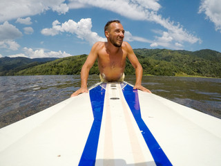 Young man paddles on a long-board in lake.