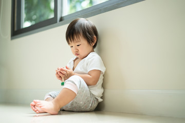 Asian cute baby sitting and playing a small toy sitting alone on floor at home. The kid holding the toy and question about how to play it. Play and learn of young child education concept