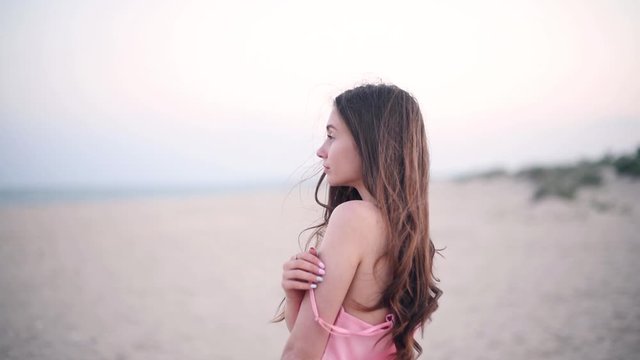 Young pretty girl with long bunette hair and blue eyes staying with denuded shoulder against the sea