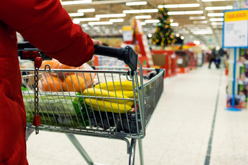 Woman with a basket walks in a supermarket. Hand and part of the basket in focus, blurred background