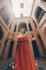 a girl in a bright dress of the peoples of Morocco stands arms outstretched and raised her head up in the middle of a religious building - 307689746