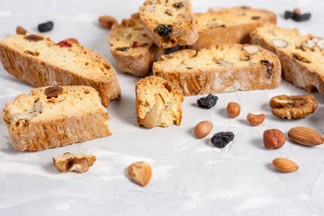 Tasty traditional Italian homemade biscotti or cantuccini cookies with hazelnuts, almonds, raisins and walnuts on a light gray background.
