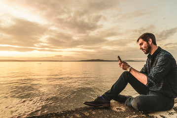 Man using smart phone while relaxing water at sunset.