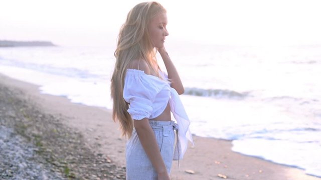 Beautiful blonde woman in a white blouse walking at the sea