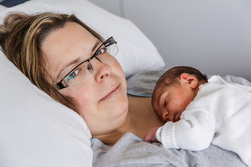 mujer madre con bebé hijo recién nacido (neonato) dormido haciendo el piel con piel en la cama...
