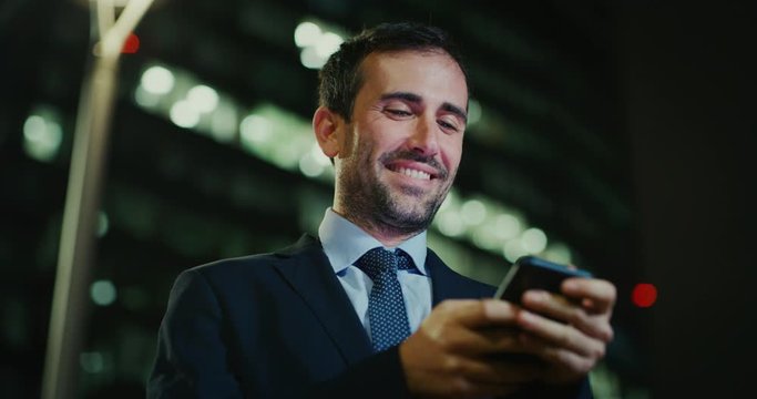 Slow motion of an young handsome businessman is using a smartphone in a busy city center with traffic by night . Shot in 8K. Concept of business and finance, success, monopoly,wall street