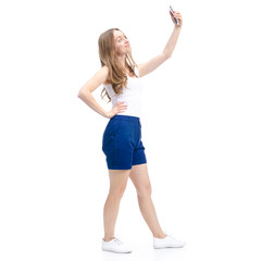 Fototapeta premium Woman in blue shorts and white shirt standing, smiling, making selfie on smartphone on white background isolation