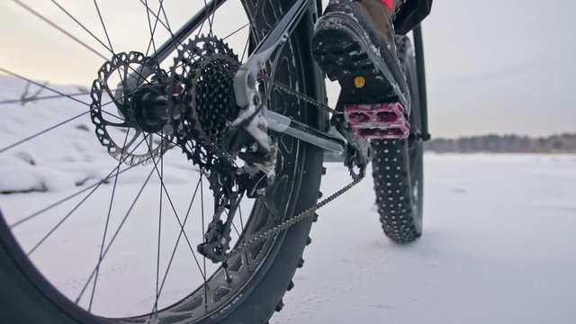 Professional extreme sportsman biker riding fat bike in outdoors. Cyclist ride in winter snow forest. Man does trial trick wheelie on mountain bicycle with big tire in helmet and glasses.