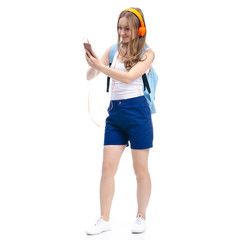 Woman in blue shorts and white shirt with blue backpack student standing smiling looking, listening to music on headphones, smartphone on white background isolation