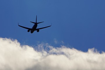 Fototapeta na wymiar Silhouette of plane on blue sky flying towards white clouds