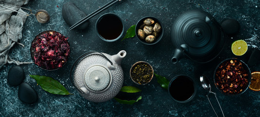 Set of black, green, fruit and herbal tea on black stone background. Tea in teapot and cup. Top...