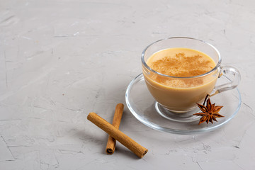 Masala tea in a glass cup with anise, cinnamon and ginger on a gray background