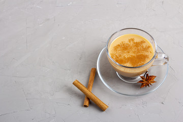 Masala tea in a glass cup with anise, cinnamon and ginger on a gray background