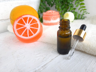 Spa aromatherapy citrus concept. Close up bottle with dropper, orange soap,towel on white wooden background. Copy space. Selective focus.