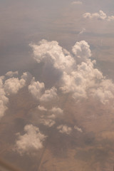 Fototapeta na wymiar View of the clouds from airplane window flying high showing land below