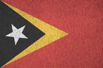 Timor Leste flag depicted in bright paint colors on old relief plastering wall. Textured banner on...