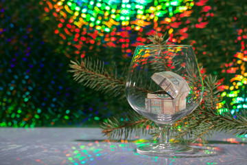 An open chest with gifts stands in a wine glass. Against the background of a fir branch and rainbow bokeh.