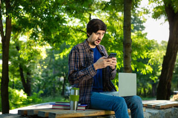 Young freelancer sitting with a laptop and coffee in a park. Work at any place