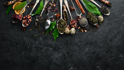 Set tea in spoons. Black, green, fruit and white tea. On a black stone background. Top view. free...