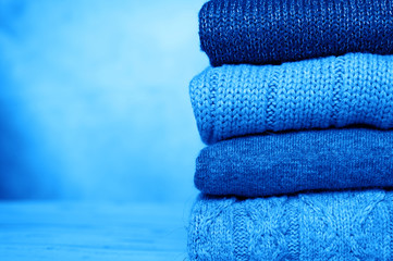 a stack of knitted winter sweaters in several shades of dark blue on concrete background. classic...