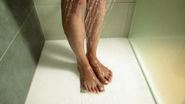 Young beautiful woman taking a shower in a bathroom. Close-up shot of female legs. Slow motion. HD