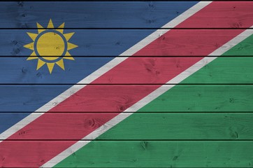 Namibia flag depicted in bright paint colors on old wooden wall. Textured banner on rough background