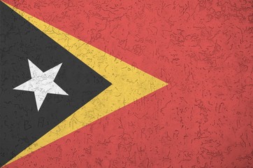 Timor Leste flag depicted in bright paint colors on old relief plastering wall. Textured banner on...