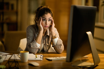 Young woman reading confusing e-mail on desktop PC at night.