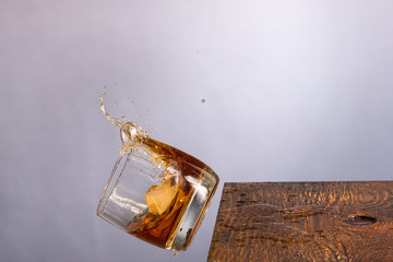 falling glass with whiskey with ice with splashes on a wooden background