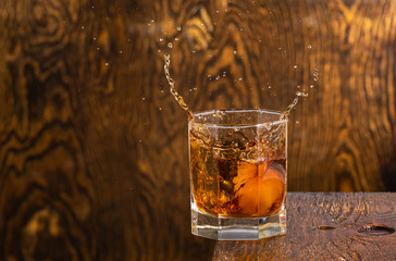 glass with whiskey and falling ice with splashes on a wooden background