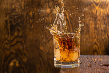 glass with whiskey and falling ice with splashes on a wooden background