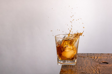 falling glass with whiskey with ice with splashes on a wooden background