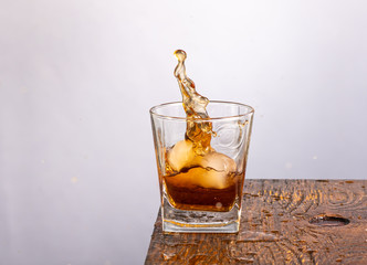 ice falls into a glass standing on the edge with whiskey and splashing on a gray background