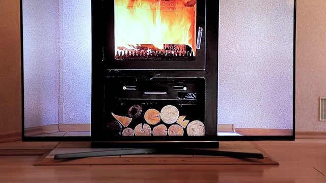 The television with the video of the burning stove stands before the stove in the apartment. The TV screen imitates the fire in the fireplace stove.