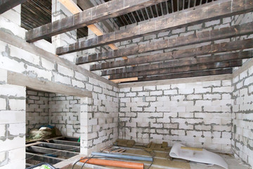 Construction site of residential building interior in progress to new house. Empty room with doorway, wooden beams for ceiling or roof and white brick wall