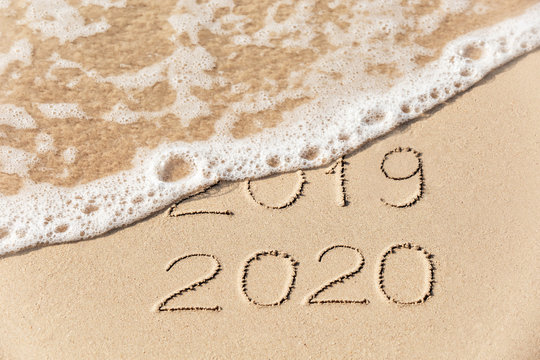2020 2019 inscription written in the wet yellow beach sand being washed with sea water wave