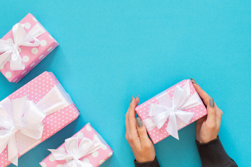 Girl holds gift box, pink gift boxes in polka dots with white ribbon and bow on a blue background , flat lay, top view, birthday or valentines day