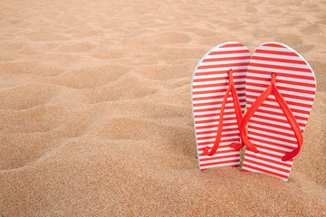 Red slippers in yellow sand on a beach near the sea, summer vacation